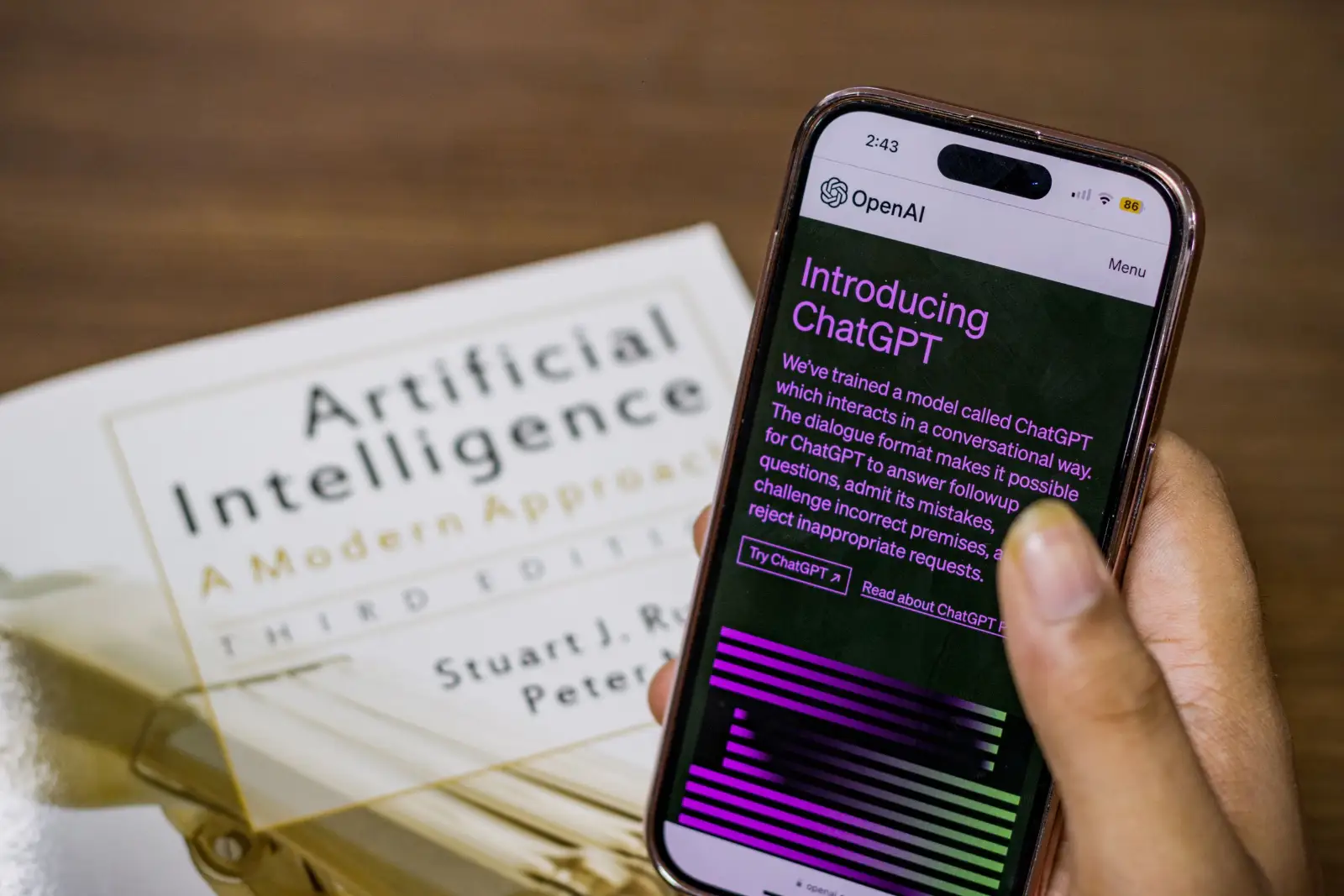 Smartphone showing ChatGPT held above an artificial intelligence textbook