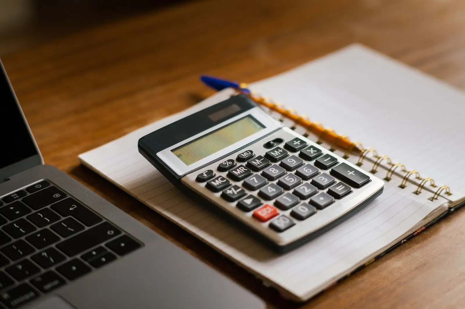 Calculator and notebook on a desk beside a laptop